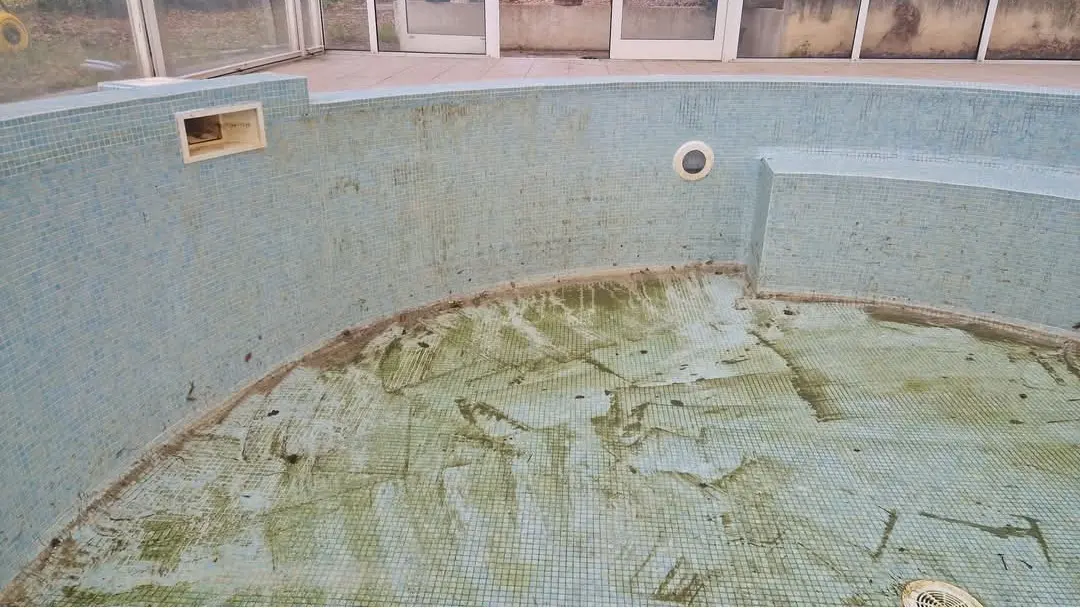 Avant nettoyage d’une piscine couverte Piscine couverte avant intervention de nettoyage avec bassin vidé présentant des salissures, algues et dépôts.